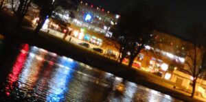 Eine Stadt am Ufer bei Nacht mit bunten Lichtspiegelungen in einem Fluss.