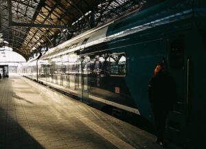 Zug im Bahnhof, vor dem eine Zugbegleiterin steht.